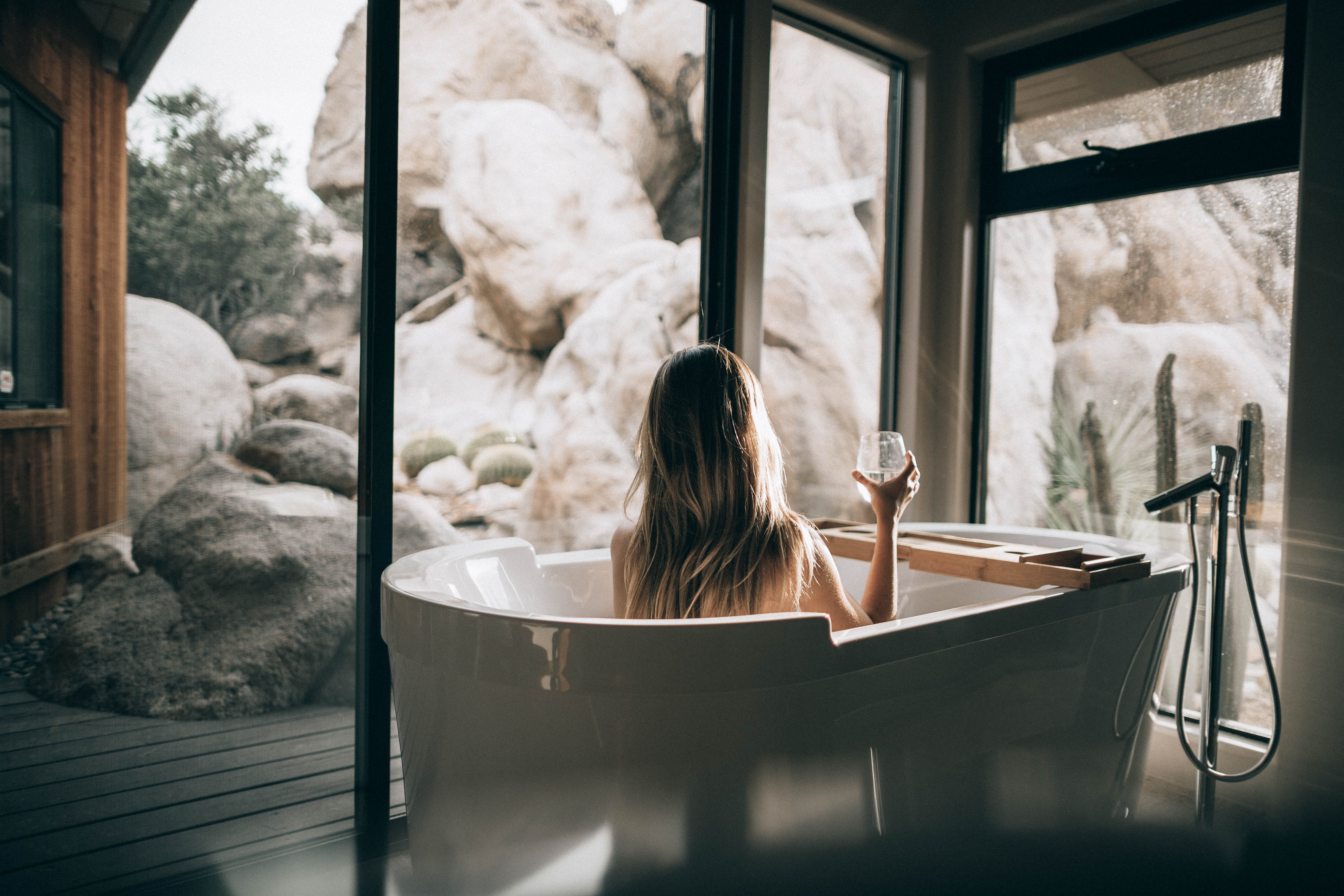 Young Woman Enjoying a Glass of Wine in a Modern Bathtub Overlooking a Peaceful Landscape